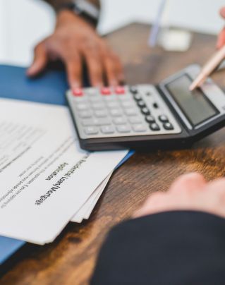 Hands using a calculator with real estate documents on a desk, indicating a financial transaction or meeting.